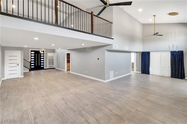 unfurnished living room featuring visible vents, baseboards, a high ceiling, and ceiling fan