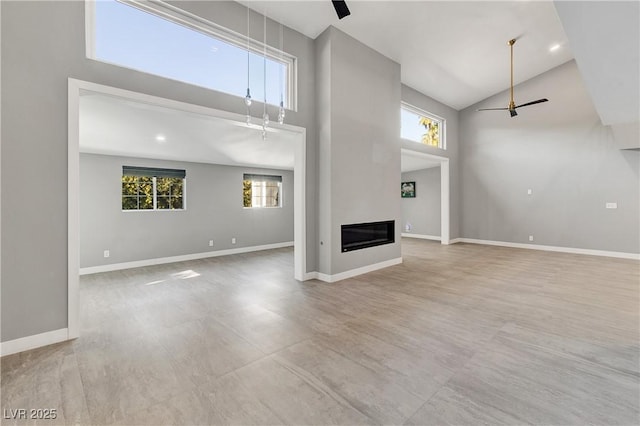 unfurnished living room featuring a glass covered fireplace, high vaulted ceiling, baseboards, and ceiling fan