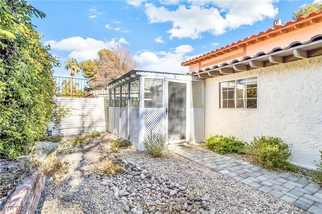 view of side of property featuring stucco siding, a tiled roof, and fence