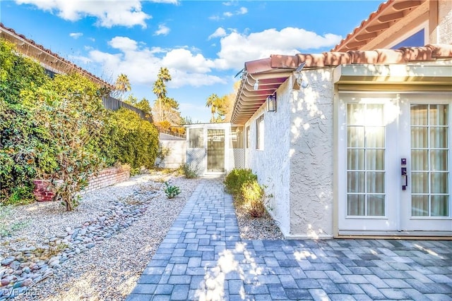 view of property exterior with a patio area, stucco siding, french doors, and fence