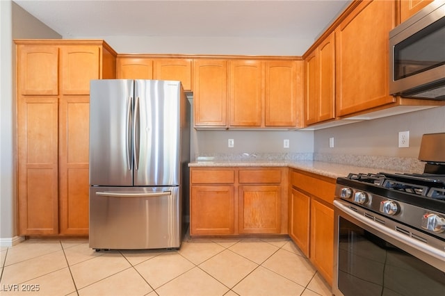 kitchen featuring light tile patterned flooring, appliances with stainless steel finishes, and light stone counters