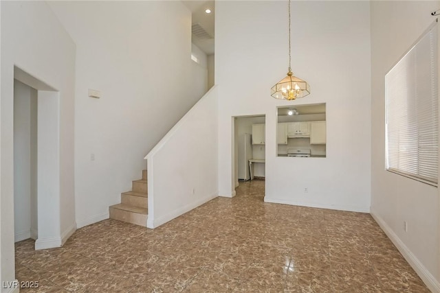 unfurnished living room with baseboards, a notable chandelier, a towering ceiling, and stairs