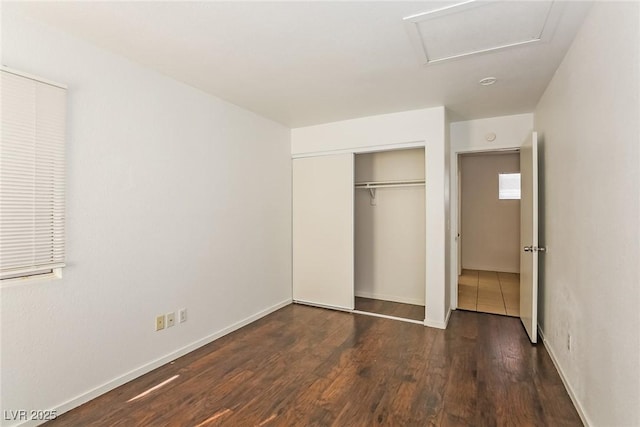 unfurnished bedroom featuring attic access, wood finished floors, a closet, and baseboards