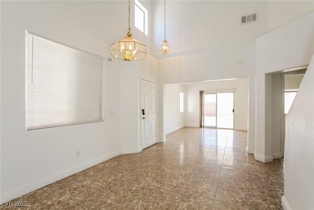 unfurnished room featuring an inviting chandelier, a healthy amount of sunlight, visible vents, and a towering ceiling