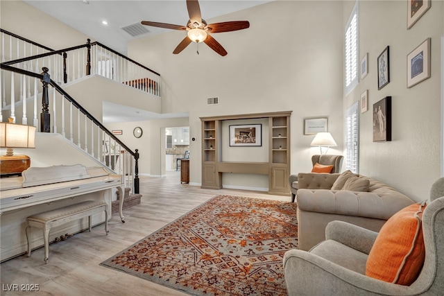 living area with wood finished floors, stairway, a ceiling fan, and visible vents