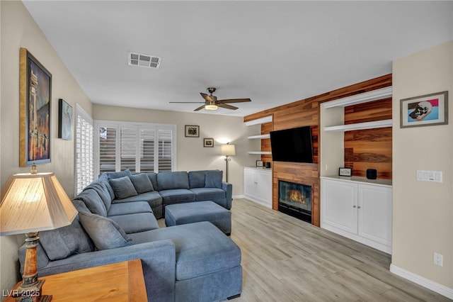 living area with visible vents, a large fireplace, baseboards, wood finished floors, and a ceiling fan