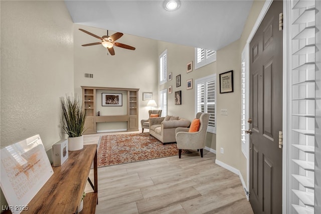 entryway with visible vents, light wood-style flooring, a ceiling fan, and a towering ceiling