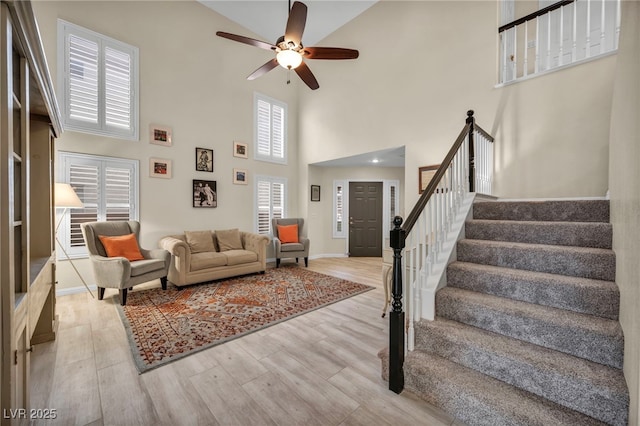 living area with baseboards, a ceiling fan, wood finished floors, and stairs