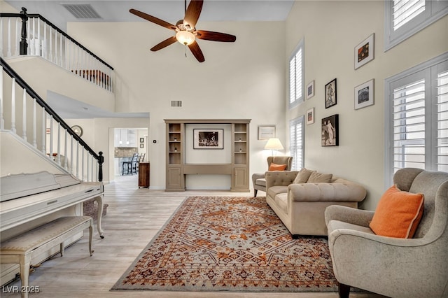 living room featuring light wood-type flooring, visible vents, ceiling fan, and stairway