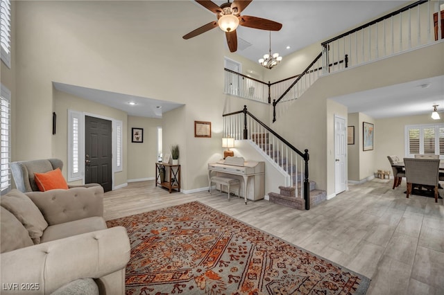 living room with ceiling fan with notable chandelier, wood finished floors, baseboards, a towering ceiling, and stairs