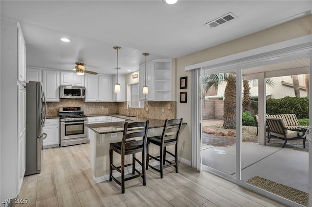 kitchen featuring visible vents, a peninsula, a sink, stainless steel appliances, and white cabinets