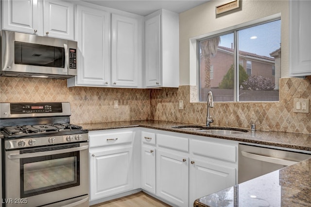 kitchen with a sink, dark stone countertops, tasteful backsplash, white cabinetry, and appliances with stainless steel finishes