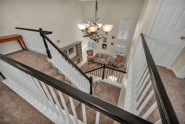 stairs with visible vents, baseboards, carpet floors, a high ceiling, and a notable chandelier