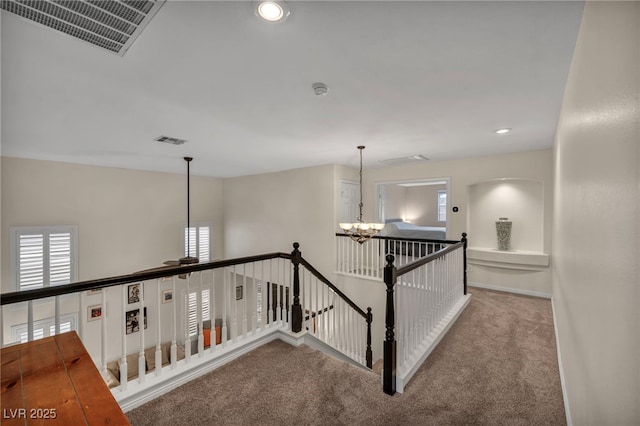 hallway featuring an upstairs landing, visible vents, carpet, and an inviting chandelier