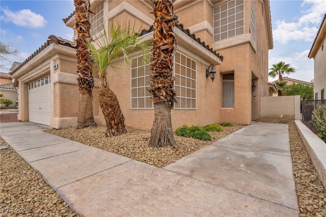 view of home's exterior with stucco siding, a garage, and fence