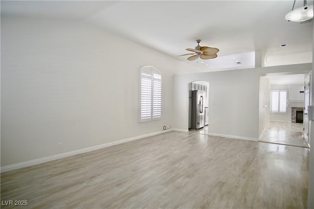 spare room featuring light wood-type flooring, arched walkways, baseboards, ceiling fan, and vaulted ceiling