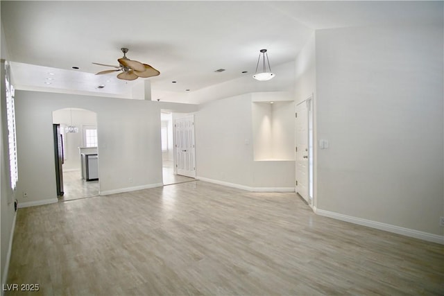 unfurnished living room with baseboards, arched walkways, a ceiling fan, and light wood finished floors