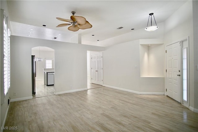 unfurnished living room with arched walkways, baseboards, light wood-type flooring, and ceiling fan