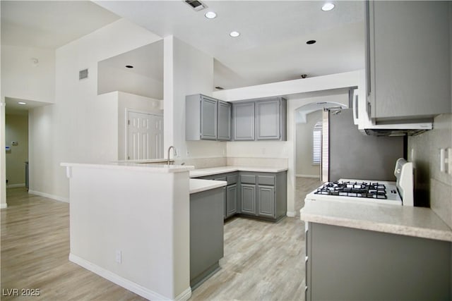 kitchen featuring a peninsula, white gas stove, arched walkways, gray cabinetry, and light wood-type flooring