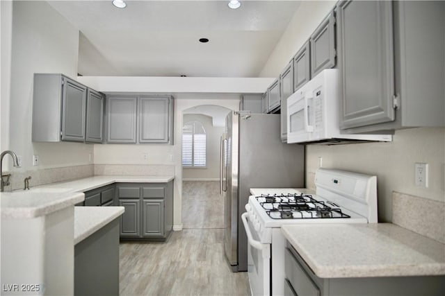 kitchen with white appliances, light wood finished floors, arched walkways, gray cabinets, and light countertops