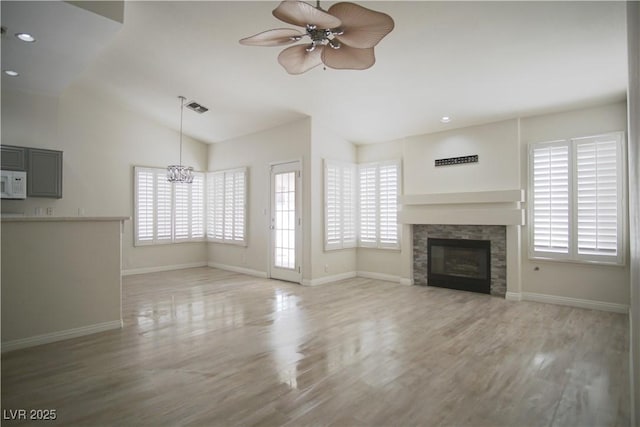 unfurnished living room featuring lofted ceiling, wood finished floors, ceiling fan with notable chandelier, and visible vents