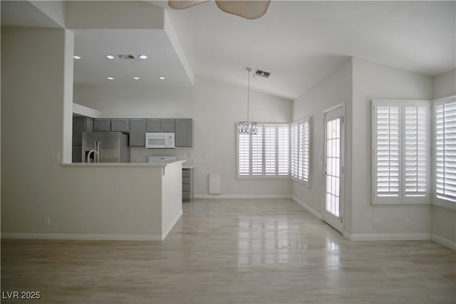 unfurnished living room featuring visible vents, baseboards, light wood-type flooring, lofted ceiling, and ceiling fan with notable chandelier