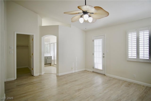 interior space featuring a ceiling fan, baseboards, lofted ceiling, arched walkways, and light wood-type flooring