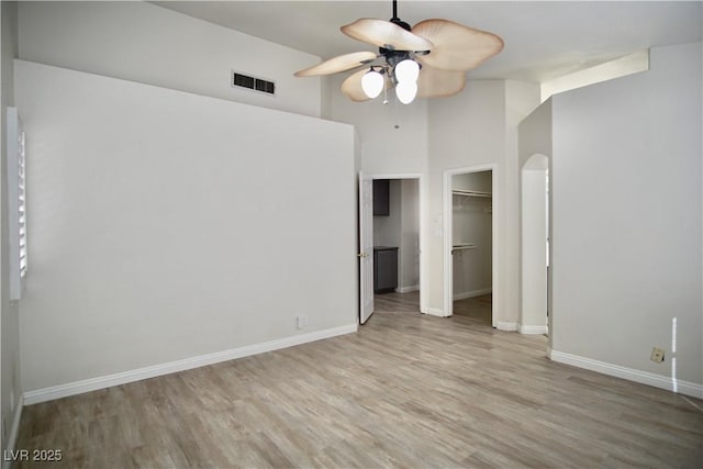 unfurnished bedroom featuring wood finished floors, arched walkways, visible vents, and baseboards