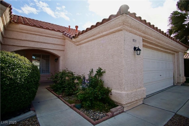 view of side of home with a tiled roof, an attached garage, and stucco siding