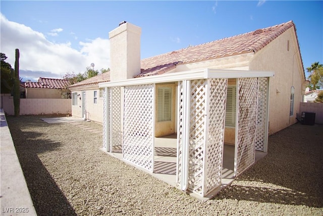 rear view of house with fence, central AC, stucco siding, a chimney, and a tile roof