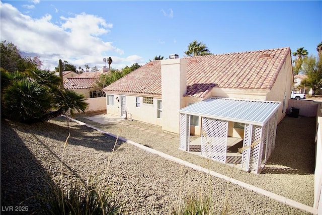 rear view of property with stucco siding, a chimney, and a tiled roof