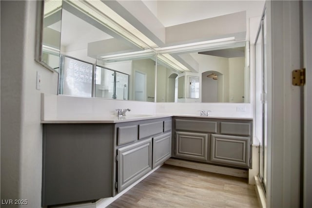 full bath with double vanity, a sink, a stall shower, and wood finished floors