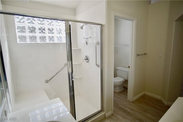 full bath featuring baseboards, toilet, wood finished floors, and a shower stall