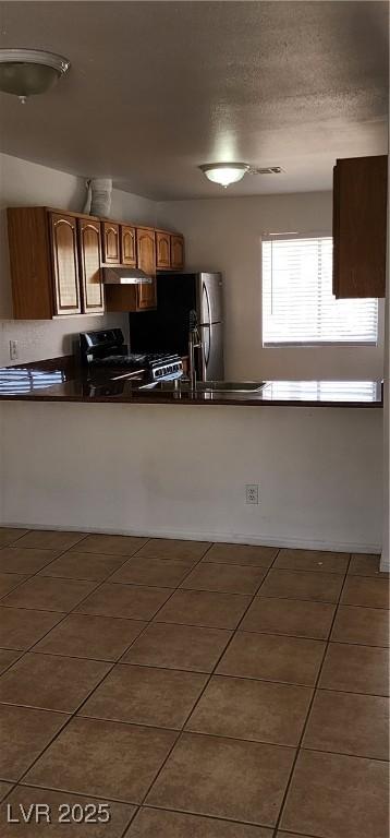 510 Holick Ave, Henderson, NV 89011 - kitchen featuring tile patterned floors, under cabinet range hood, dark countertops, and freestanding refrigerator