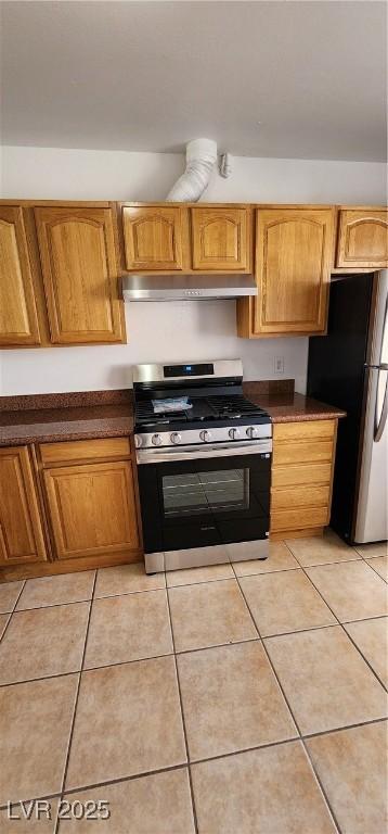 510 Holick Ave, Henderson, NV 89011 - kitchen with stainless steel gas stove, under cabinet range hood, freestanding refrigerator, dark countertops, and light tile patterned flooring
