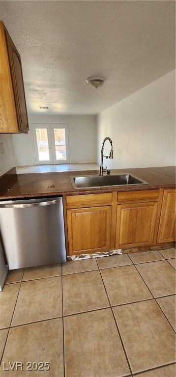 510 Holick Ave, Henderson, NV 89011 - kitchen with stainless steel dishwasher, brown cabinets, light tile patterned floors, dark countertops, and a textured ceiling