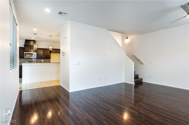 unfurnished living room featuring visible vents, stairs, baseboards, and wood finished floors