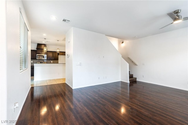 unfurnished living room featuring visible vents, wood finished floors, baseboards, ceiling fan, and stairs