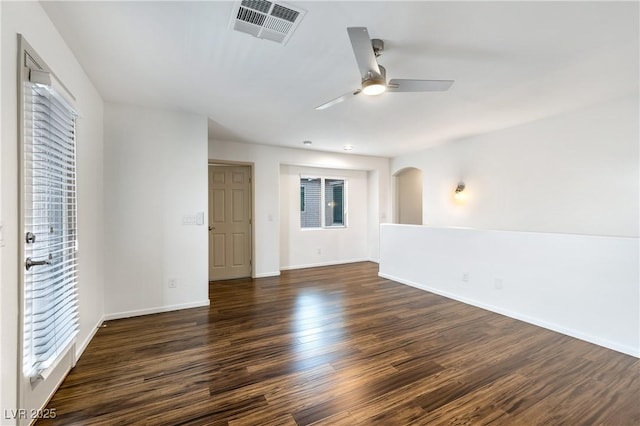 unfurnished room featuring a ceiling fan, visible vents, baseboards, arched walkways, and dark wood-type flooring