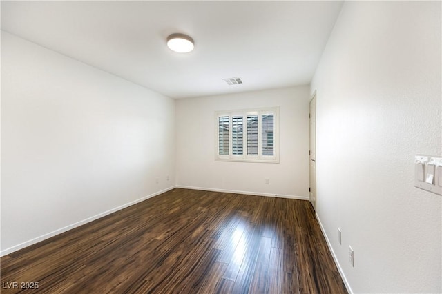 spare room featuring visible vents, baseboards, and dark wood finished floors