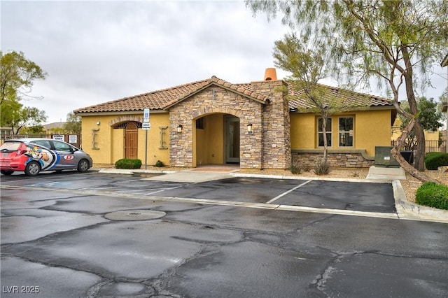 mediterranean / spanish house with stone siding, stucco siding, a tiled roof, and uncovered parking