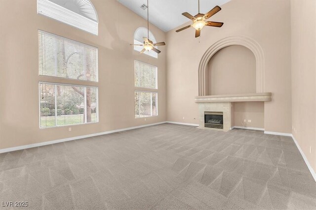 unfurnished living room featuring a ceiling fan, baseboards, carpet floors, a high ceiling, and a fireplace