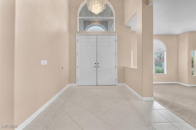 tiled foyer featuring an inviting chandelier, baseboards, and carpet floors