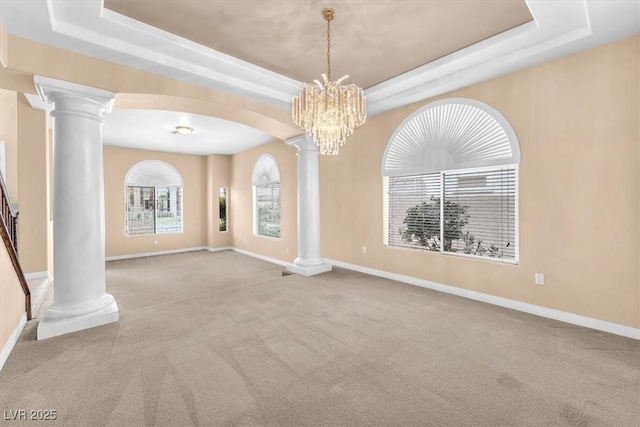 carpeted spare room featuring baseboards, decorative columns, arched walkways, a notable chandelier, and a raised ceiling