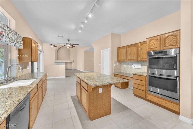 kitchen with ceiling fan, a sink, appliances with stainless steel finishes, backsplash, and a center island