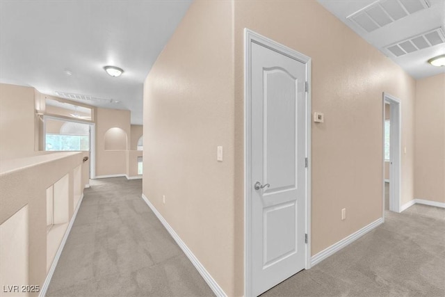 corridor with light colored carpet, visible vents, and baseboards