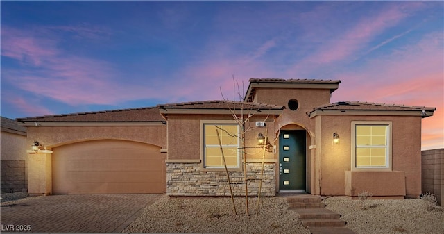 mediterranean / spanish home featuring stucco siding, a tile roof, decorative driveway, stone siding, and a garage