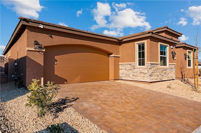 view of front of property featuring stucco siding, decorative driveway, stone siding, a garage, and a tiled roof