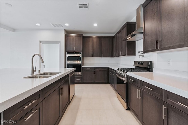 kitchen featuring visible vents, a sink, stainless steel appliances, dark brown cabinetry, and wall chimney range hood