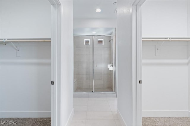 bathroom featuring a walk in closet, a shower stall, and baseboards